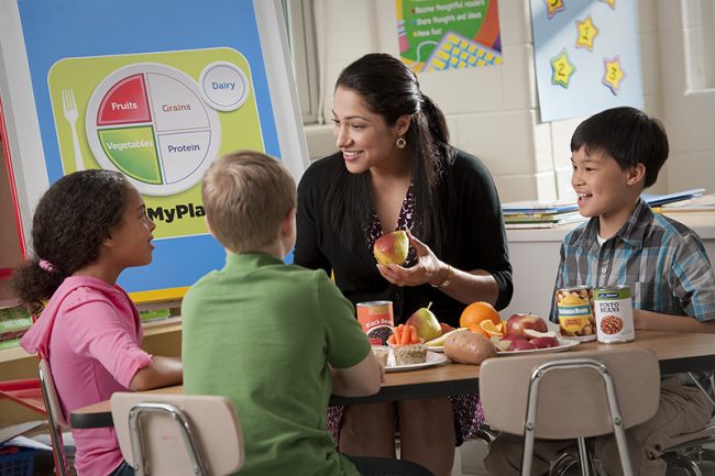 Woman teacher speaking to 3 children at a table