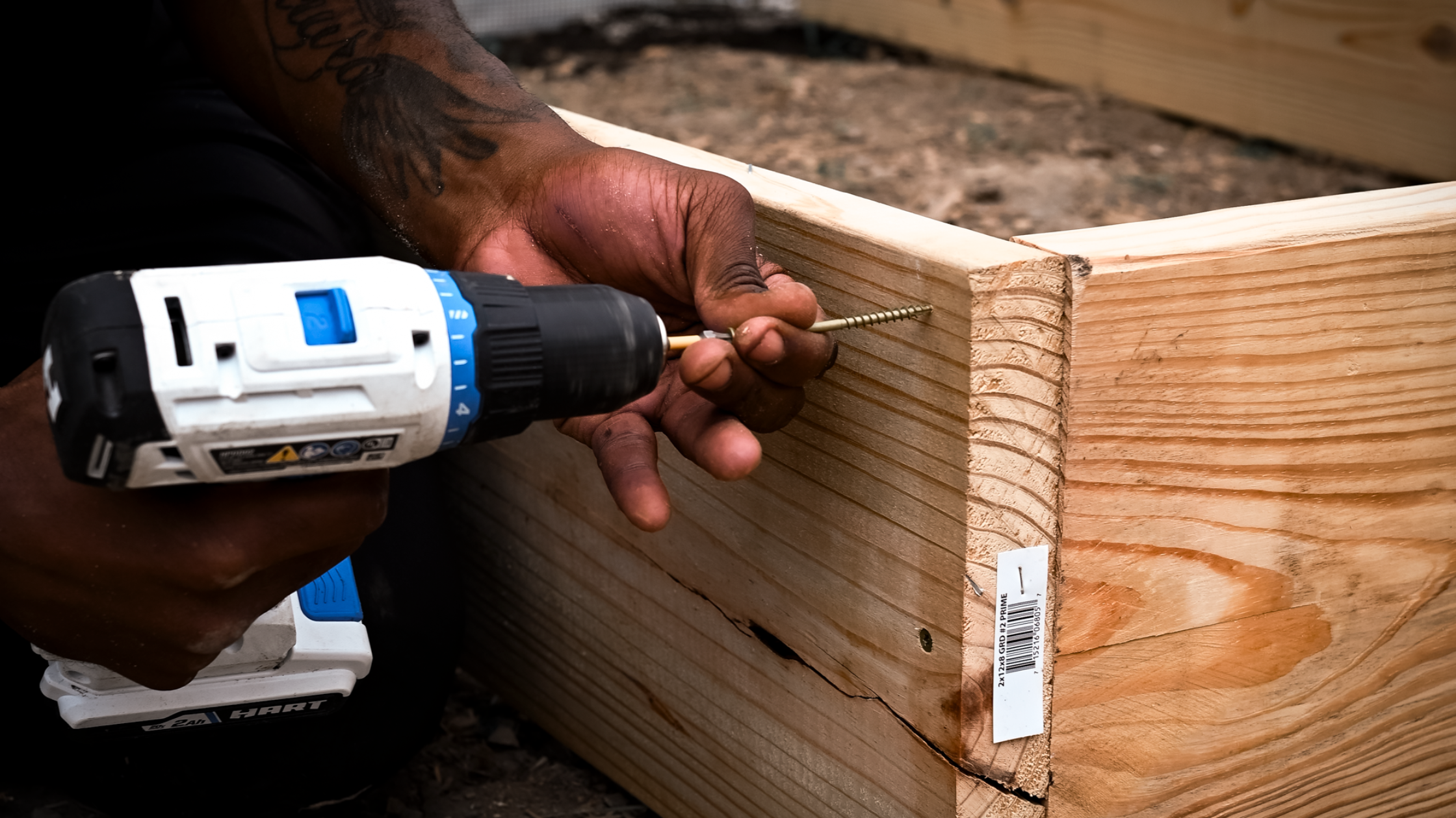 Hand holding drill and screw to screw to wooden boards together.