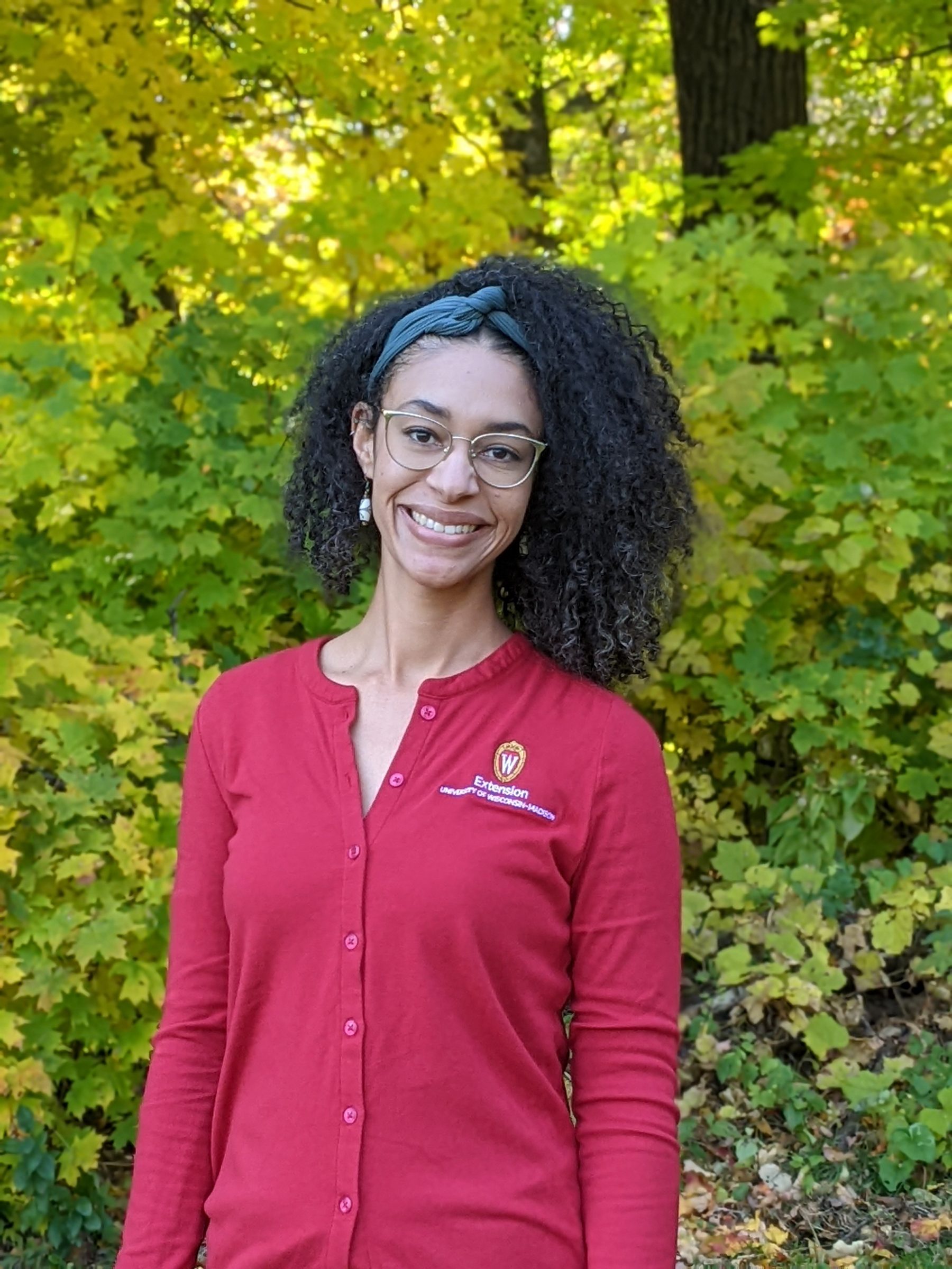 woman educator wearing a red sweater with hair down and glasses in a forest setting