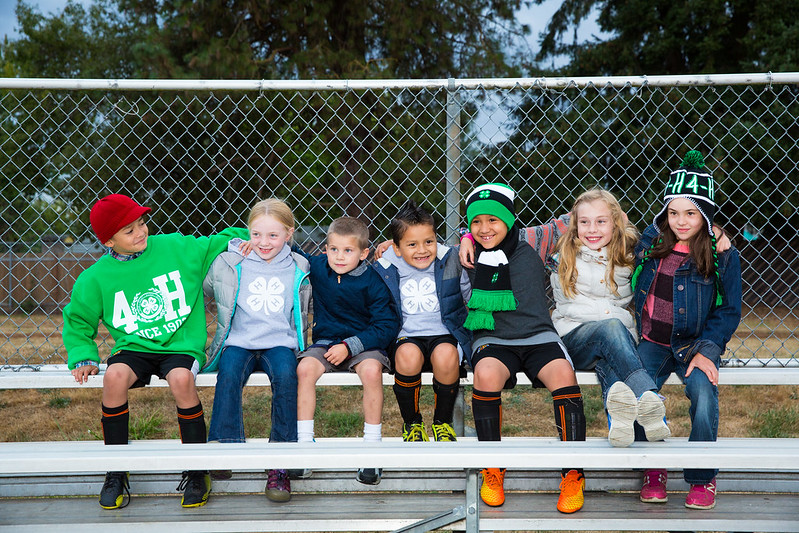 Group of 7 children sitting on a bleacher with 4-H gear in fall clothing